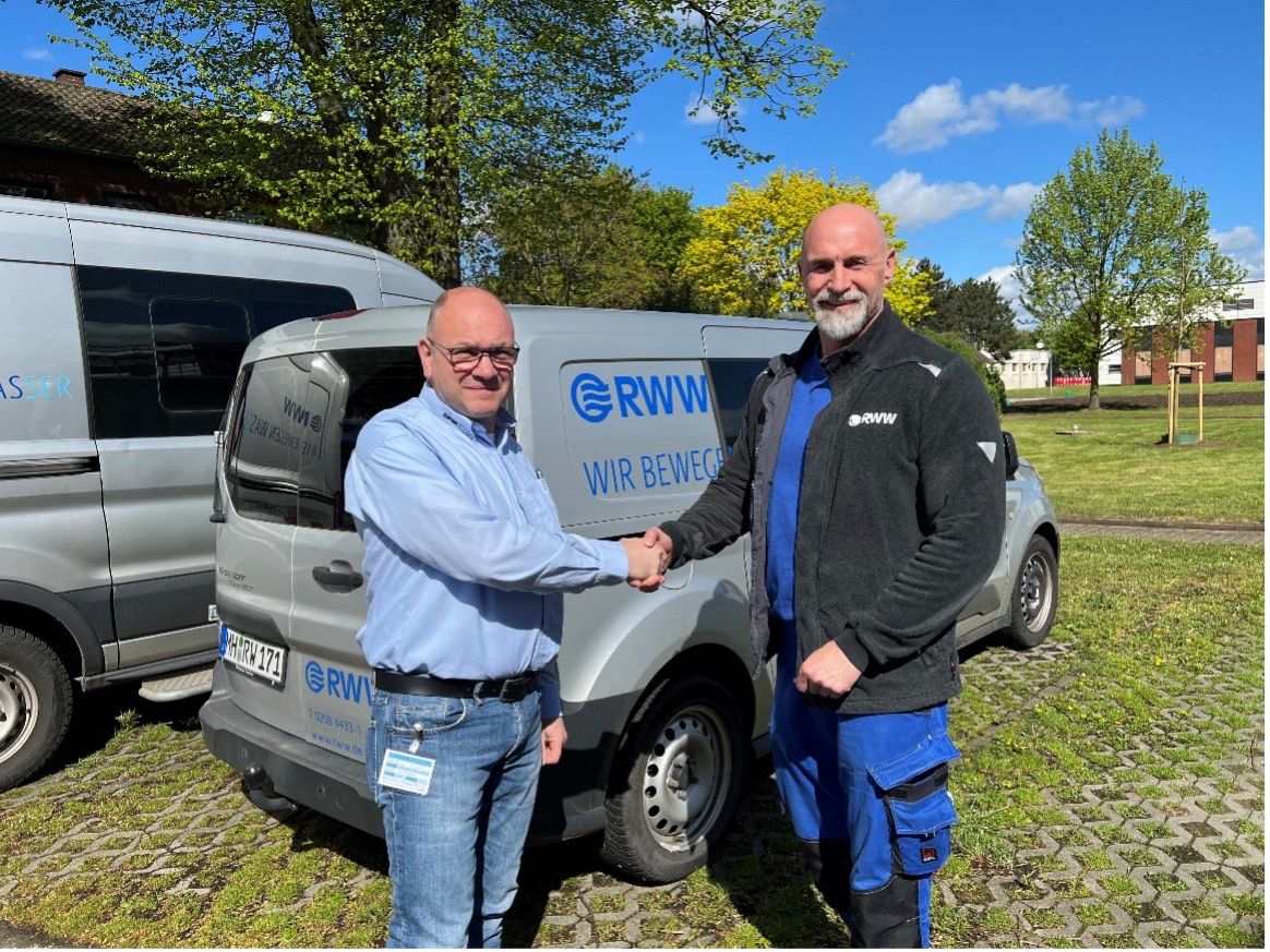 Two men shaking hands outdoors with company vehicles in the background